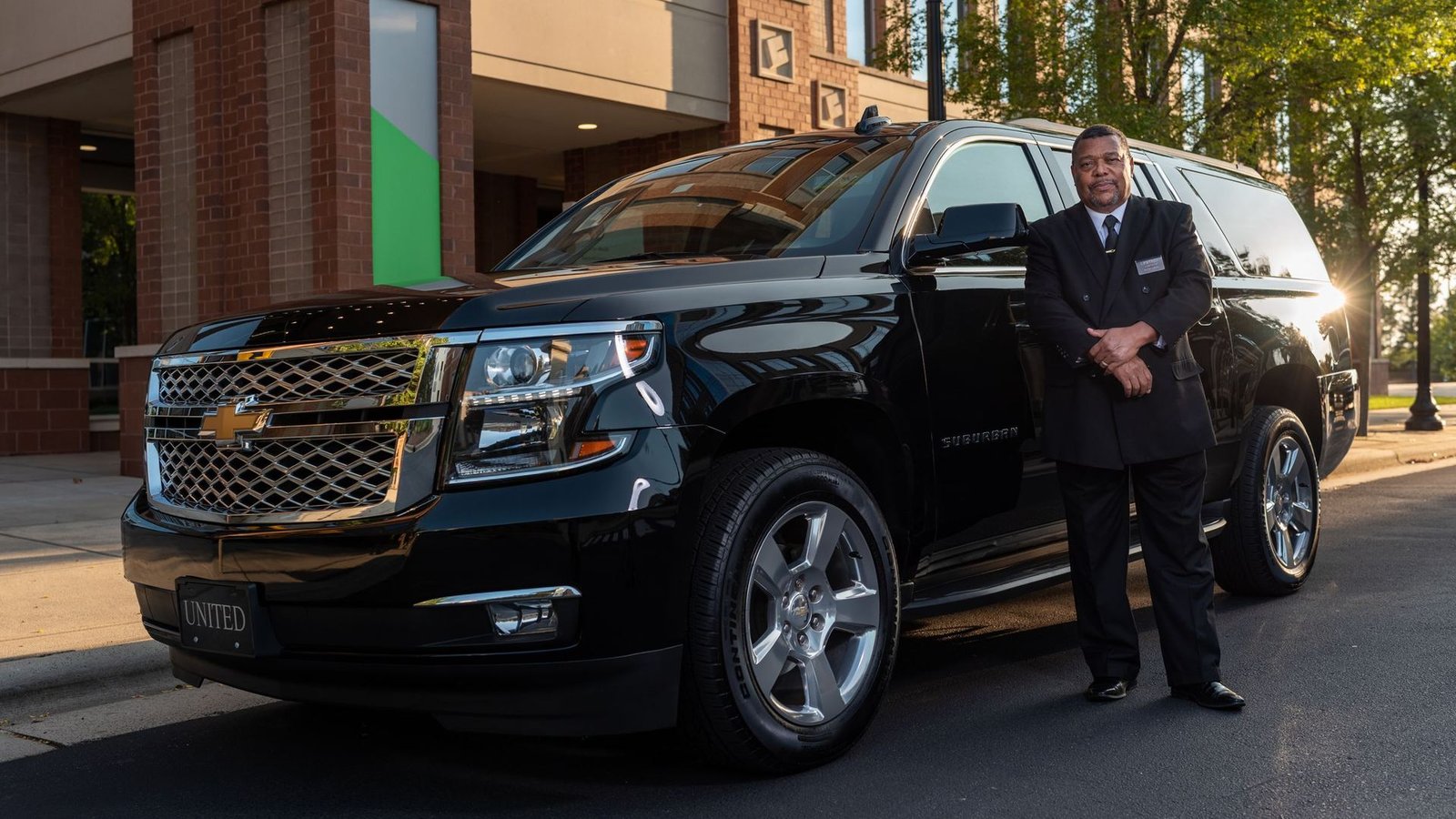 A chauffeur in a suit standing beside a black SUV