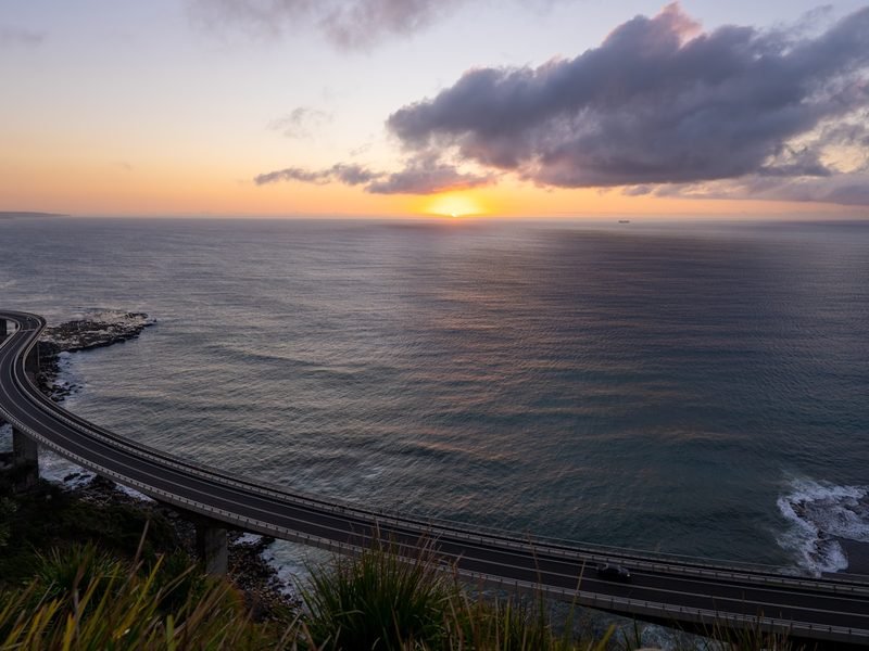 A coastal highway curving along the ocean at sunset