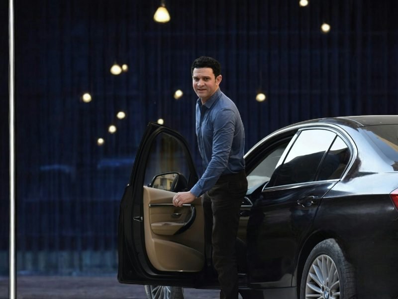 A driver holding the rear door of a dark car open at night